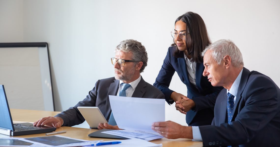 Profissionais jurídicos analisando documentos fiscais e dados em computador durante preparação de defesa tributária.