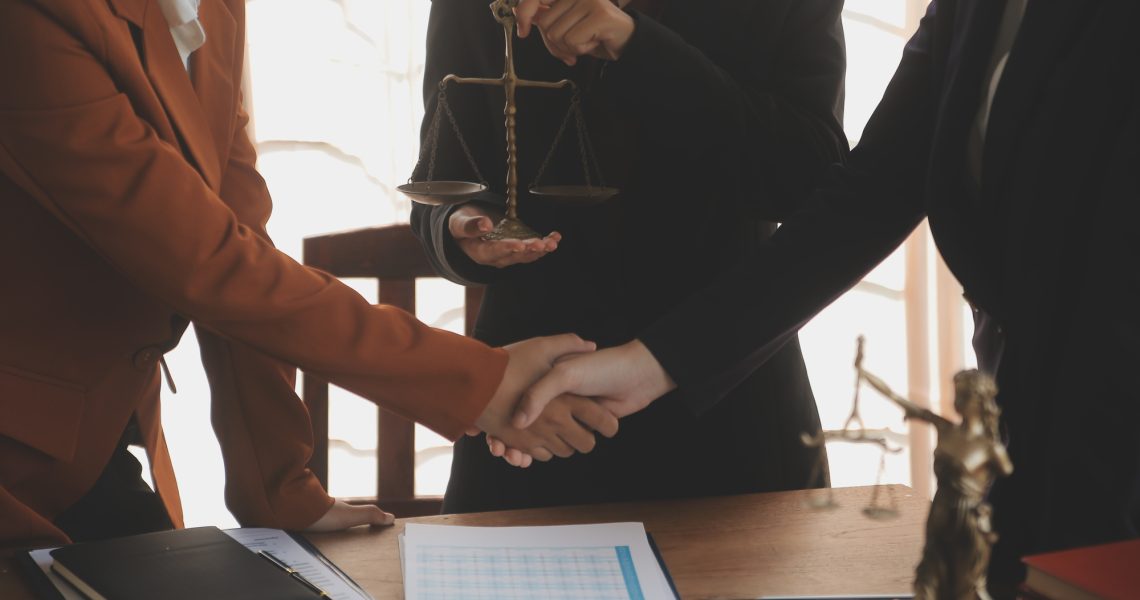Advogados realizando handshake durante processo de due diligence jurídica em fusões e aquisições, com balança da justiça ao fundo.