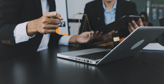 Advogados analisando documentos em notebook durante reunião estratégica sobre arbitragem empresarial como alternativa ao Judiciário.