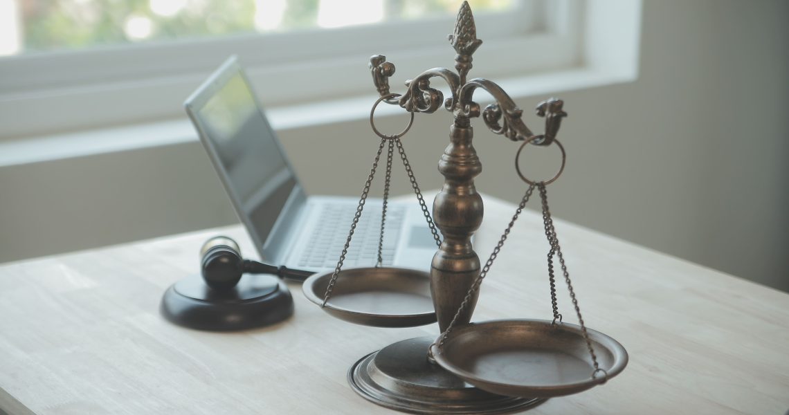 Balança da justiça, martelo jurídico e notebook sobre mesa, simbolizando a responsabilidade civil empresarial e a análise legal nas empresas.