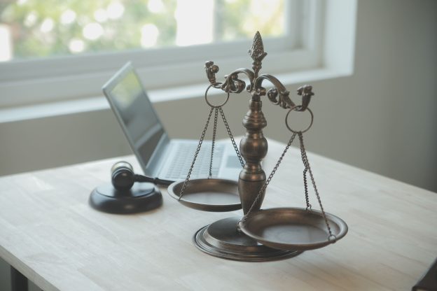 Balança da justiça, martelo jurídico e notebook sobre mesa, simbolizando a responsabilidade civil empresarial e a análise legal nas empresas.