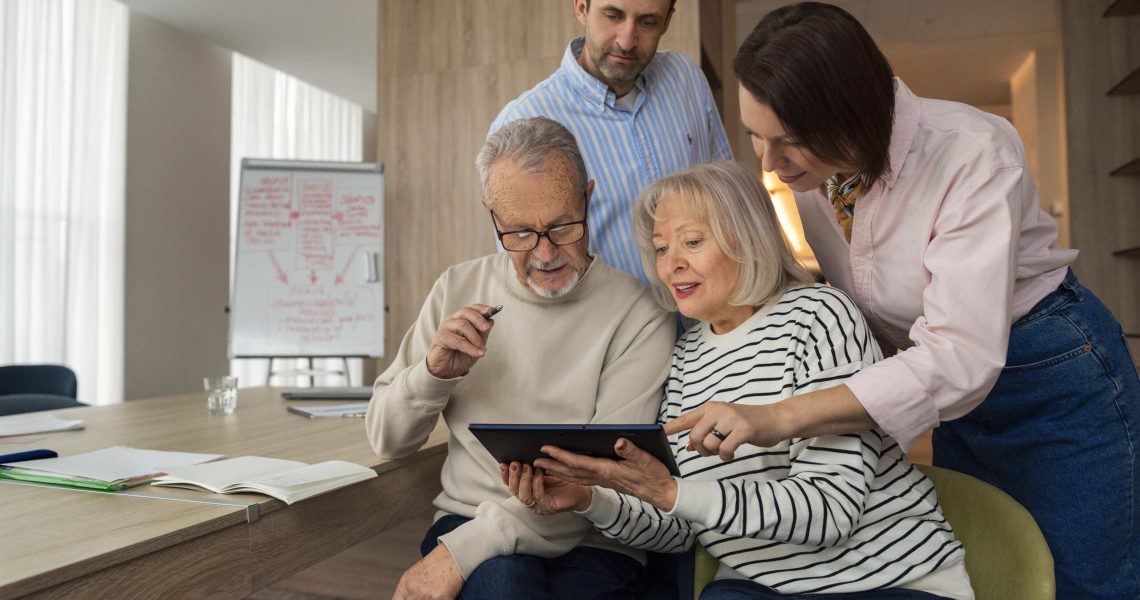 Família reunida em ambiente corporativo analisando informações em um tablet durante uma reunião de planejamento para a gestão e sucessão de uma empresa familiar.